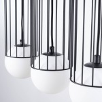 Lampa wisząca Brina 3xG9 w kolorze czarnym, z trzema białymi kloszami w kształcie kul, osadzonymi w metalowej siatce. Kable zawieszenia w czarnym kolorze. Widok z bliska, ukazujący detal konstrukcji.