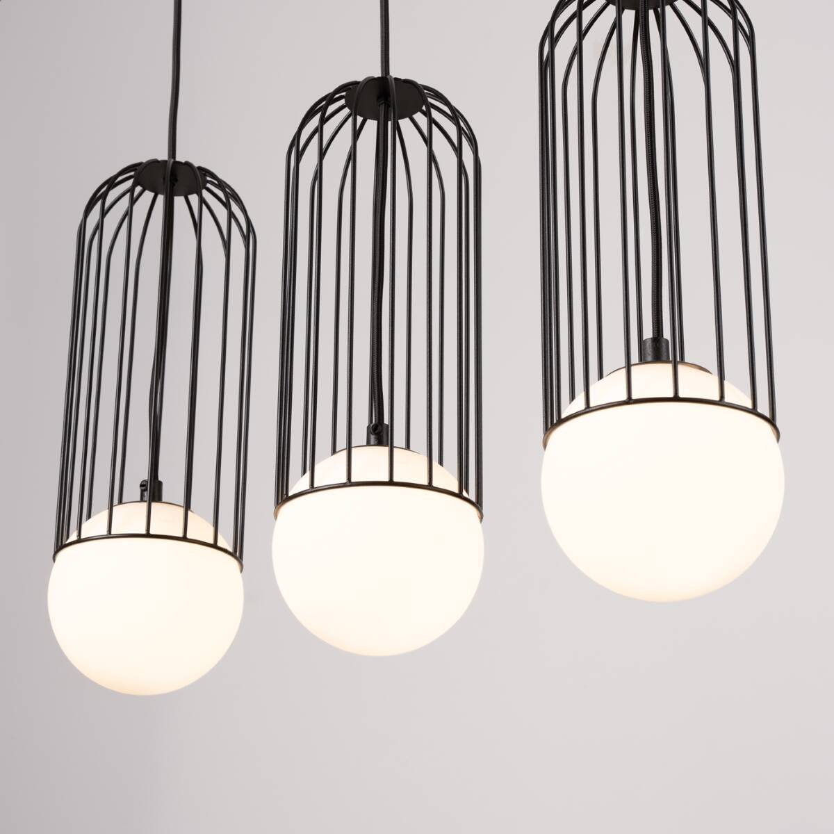 Lampa wisząca Brina 3xG9 w kolorze czarnym z metalową siatką i trzema okrągłymi kloszami z mlecznego szkła. Zawieszona na długich przewodach, w aranżacji na jednolitym tle.