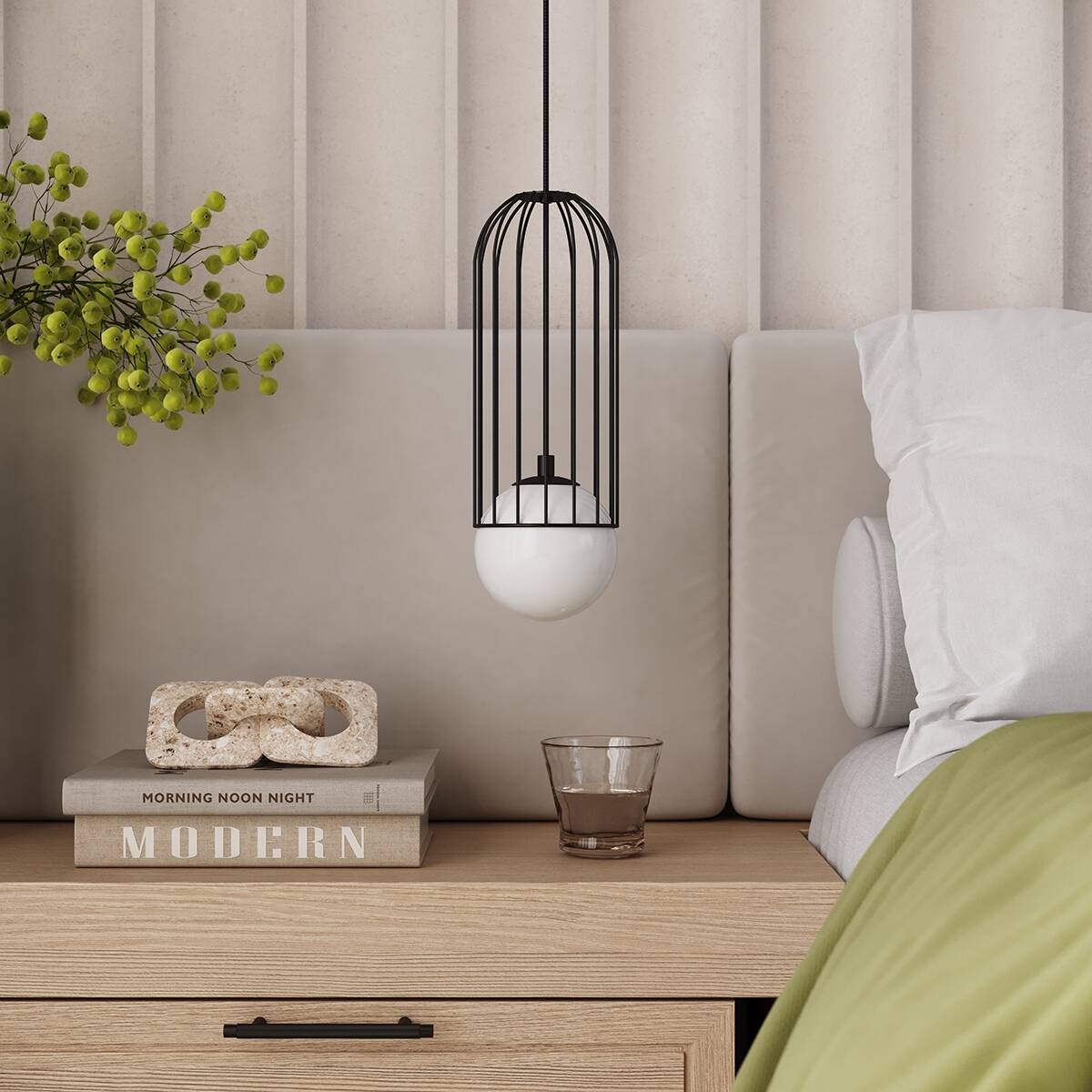 Czarna lampa wisząca Brina z kloszem w formie białej kuli, umieszczona w metalowej klatce. Wisi nad drewnianym stolikiem nocnym, obok książek i szklanki. Tło w neutralnych odcieniach, z miękką poduszką i zielonym kocem.