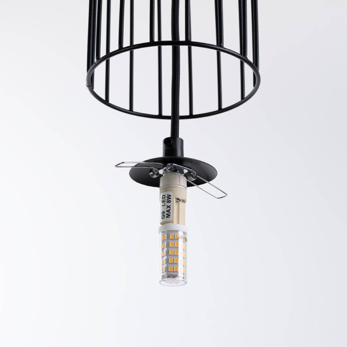 Czarna lampa wisząca Brina z metalowym, szczelinowym kloszem, z oprawką G9. Widoczny element mocujący oraz żarówka LED. Lampa zawieszona na czarnym kablu, na jednolitym białym tle.