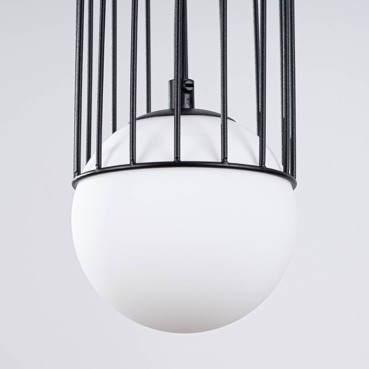 Czarna lampa wisząca Brina z kloszem w kształcie kuli, wykonana z matowego szkła, umieszczona w metalowej siatce. Ujęcie z góry, ukazujące szczegóły konstrukcji oraz połączenie klosza z zawieszeniem.