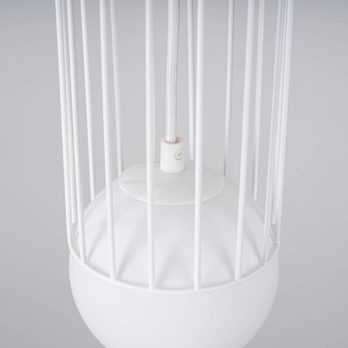Biała lampa wisząca Brina z jedną oprawą G9, z metalowym kloszem otoczonym cienkimi prętami. Widoczny detal to okrągła, matowa podstawa. Lampa zawieszona na białym przewodzie, zdjęcie ukazuje ją z góry, w zbliżeniu na elementy konstrukcyjne.