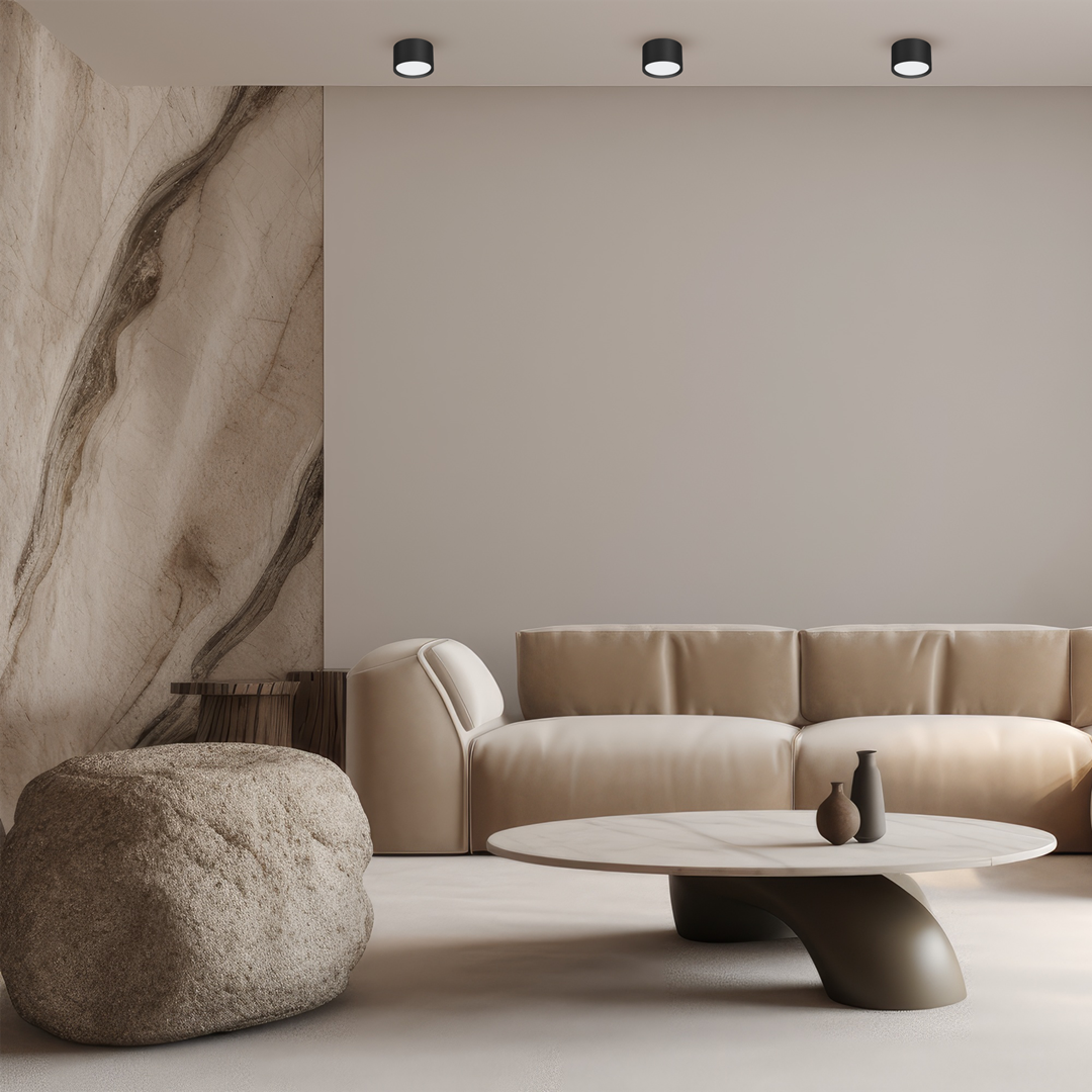 Lampa sufitowa Cyklop w kolorze czarnym, z jedną oprawą na żarówkę GX53. Zamontowana na suficie w nowoczesnym wnętrzu, w towarzystwie jasnej kanapy i okrągłego stołu. Prosta, cylindryczna forma z minimalistycznym designem.