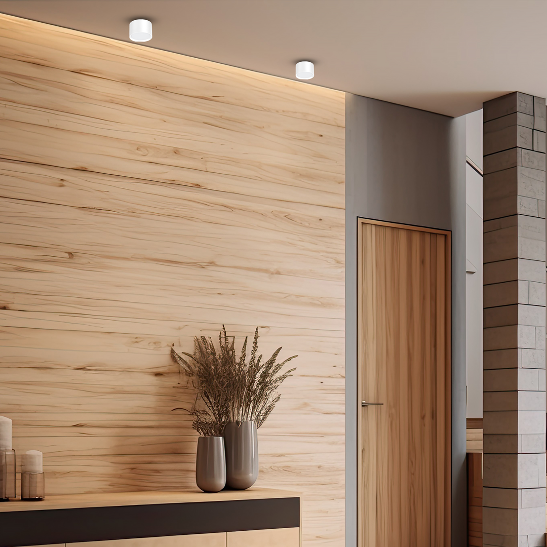 Biała lampa sufitowa Cyklop tuba 1xGX53, zamontowana na gładkim suficie w nowoczesnym wnętrzu. W tle widoczna drewniana ściana i minimalistyczne dekoracje, tworzące przytulną atmosferę. Lampa o prostym, cylindrycznym kształcie.