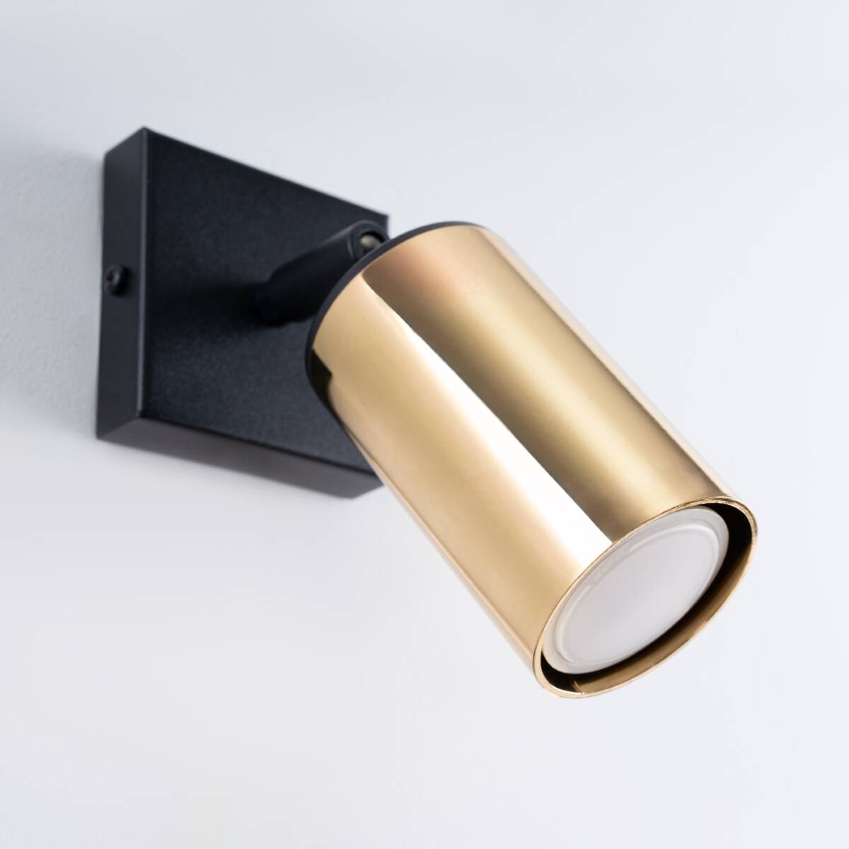 Kinkiet Winx w kolorze czarnym i złotym, z metalowym kloszem w formie walca. Uchwyt zamocowany do ściany, z widocznym źródłem światła GU10. Klosz skierowany w dół, na prostym, jasnym tle.