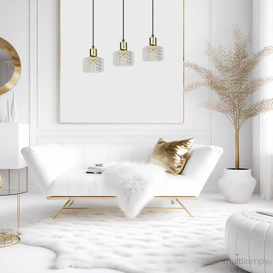 Lampa wisząca Lumi 3xG9 w kolorze czarnym i złotym, z trzema kloszami w kształcie sześcianu. Klosze wykonane z przezroczystego materiału, zawieszone na cienkich, czarnych przewodach, w nowoczesnym wnętrzu z białą sofą i złotymi akcentami.