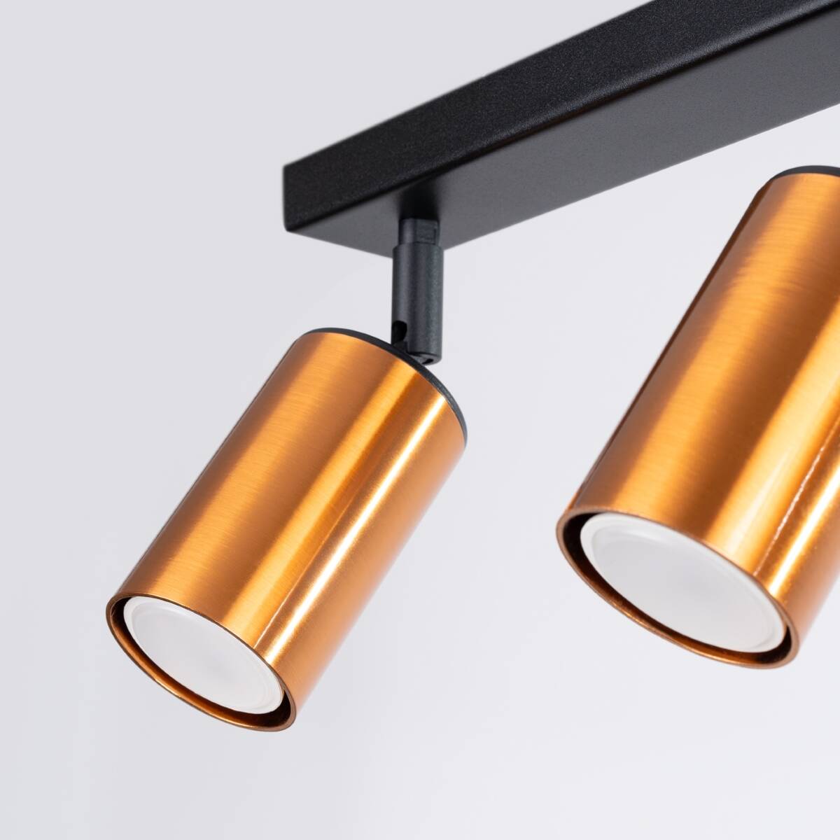 Lampa sufitowa Winx w kolorze czarnym z miedzianymi reflektorami, z dwoma punktami świetlnymi GU10. Reflektory mają cylindryczny kształt i są zamocowane na prostokątnej, czarnej podstawie. Ujęcie z bliska na detale lampy.