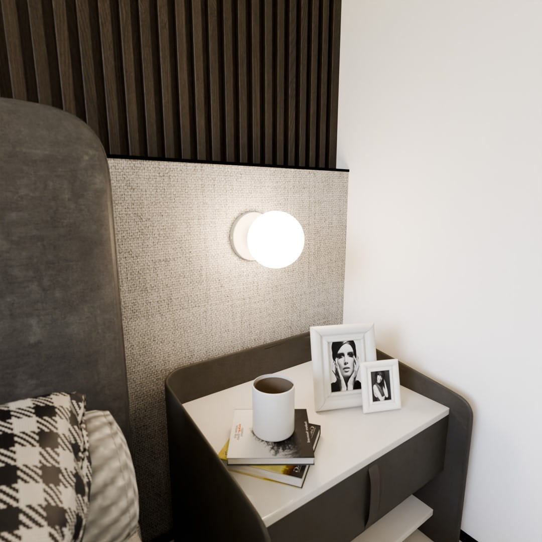 Bior kinkiet 1-punktowy w kolorze białym, zamontowany na ścianie obok łóżka. Okrągła oprawa z matowym kloszem, w otoczeniu minimalistycznych mebli oraz dekoracji na stoliku nocnym. Tło w stonowanych kolorach, z fakturą na ścianie.