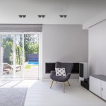 Czarna oprawa do zabudowy 1xGU10 AR111, prostokątna, zawieszona w suficie, z metalicznymi detalami. Widoczne w tle eleganckie wnętrze z fotelem i szklanymi drzwiami prowadzącymi na taras. Idealna do nowoczesnych aranżacji.