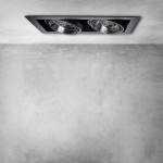 Oprawa do zabudowy Plaza 2xGU10 AR111 w kolorze czarnym, z dwoma reflektorami umieszczonymi w prostokątnej ramce. Ujęcie z góry, zamontowana w sufit, na tle szarej, gładkiej ściany.