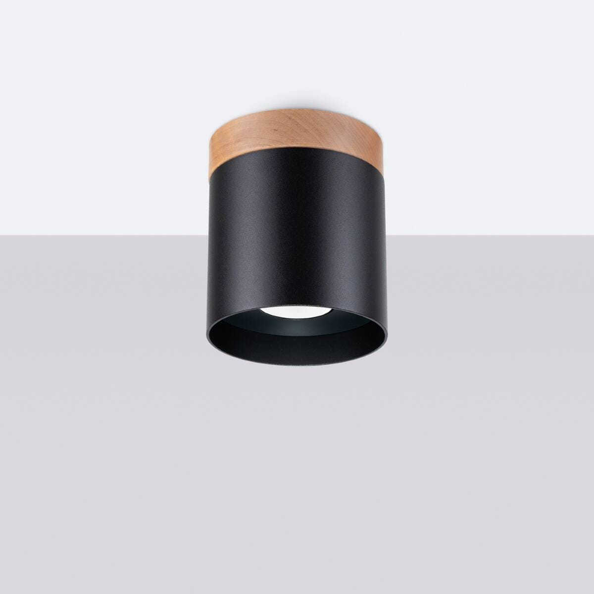 Lampa sufitowa Rif tuba w kolorze czarnym z drewnianym wykończeniem. Montowana na suficie, z cylindrycznym kształtem, posiada miejsce na żarówkę GU10. Widoczna biała oprawa wewnętrzna. Tło jasne, proste.