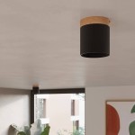 Lampa sufitowa Rif tuba 1xGU10 w kolorze czarnym z drewnianym wykończeniem. Zamontowana na suficie, okrągła forma z widocznym elementem drewnianym. Tło neutralne, minimalistyczne wnętrze z roślinnością.