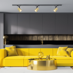 Reflektor Track Volf 1xGU10 w kolorze czarnym i złotym, zamontowany na szynie. Kąt ujęcia pokazuje trzy reflektory o cylindrycznym kształcie w nowoczesnym wnętrzu z żółtą sofą i złotym stolikiem. Tło w odcieniach szarości z elementami złotymi.