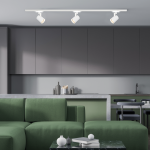 Reflektor spot Track Volf 1xGU10 w białym kolorze, zamontowany na szynie, skierowany w dół. Widoczny w nowoczesnej kuchni z zieloną sofą i szarymi meblami. Ujęcie z boku, pokazujące detale lampy i otoczenie.