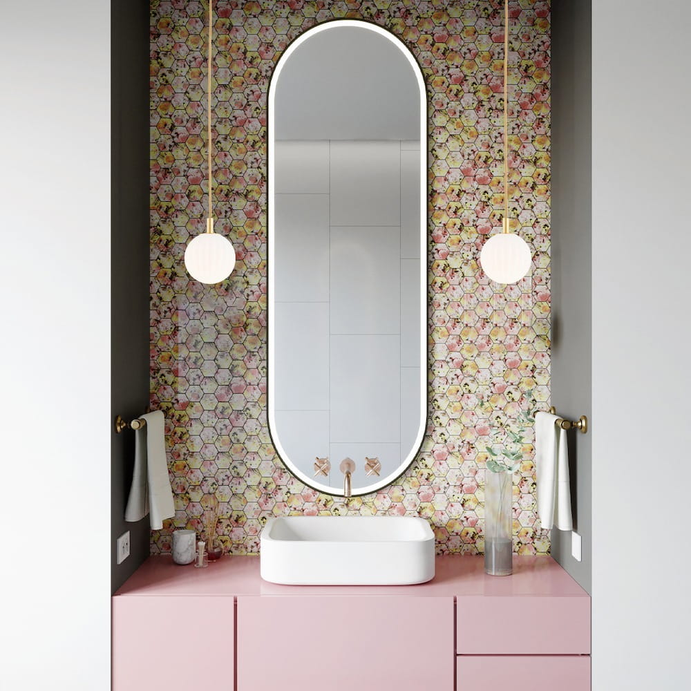 Lampa wisząca Paloma D12 z mosiężnym detalem i białym kloszem, zawieszona na długim przewodzie w łazience z kolorową, kwiatową tapetą. Produkt umieszczony obok prostokątnego lustra i umywalki na różowej szafce.