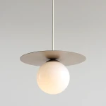 Lampa wisząca Loop Beige S z jednym gniazdem E14, z kulistym kloszem w matowym białym kolorze, zawieszona na białym przewodzie. U góry znajduje się okrągła, płaska podstawa w odcieniu beżowym. Tło jasnoszare.