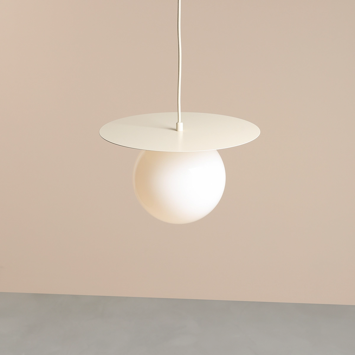 Lampa wisząca Loop Cream M z białym, półprzezroczystym kloszem w kształcie kuli, zawieszona na cienkim, białym przewodzie. Górna część w formie okrągłej płyty w kolorze kremowym. Prosta forma, idealna do nowoczesnych wnętrz.