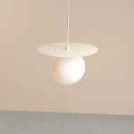 Lampa wisząca Loop Cream M z białym, półprzezroczystym kloszem w kształcie kuli, zawieszona na cienkim, białym przewodzie. Górna część w formie okrągłej płyty w kolorze kremowym. Prosta forma, idealna do nowoczesnych wnętrz.