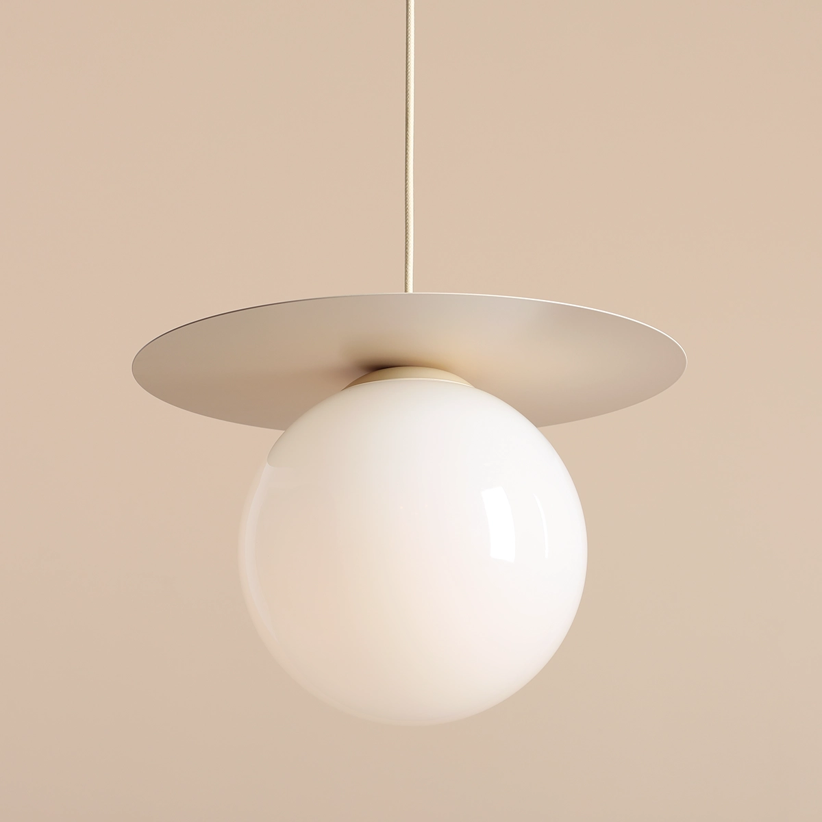 Lampa wisząca Loop Cream M wyposażona w jeden trzonek E27, z okrągłym, mlecznobiałym kloszem i metalowym, płaskim daszkiem. Produkt zawieszony na cienkim przewodzie, w kolorze beżowym, na jednolitym tle.