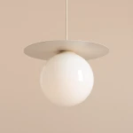 Lampa wisząca Loop Cream L z białym, okrągłym kloszem i metalowym, płaskim daszkiem. Ujęcie z góry, zawieszona na cienkim kablu. Tło w jasnym odcieniu, co podkreśla elegancję lampy. Przeznaczona do jednego źródła światła E27.