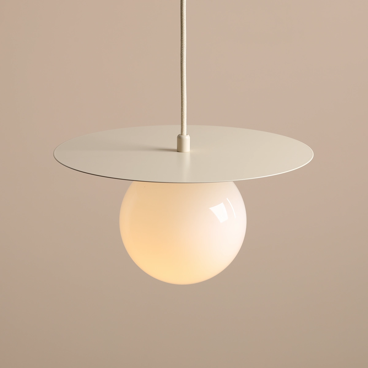 Lampa wisząca Loop Cream S z okrągłym, matowym kloszem w kolorze mlecznym oraz dużą, płaską podstawą w jasnym odcieniu. Ułożona pionowo, zawieszona na białym przewodzie, idealna do nowoczesnych wnętrz.