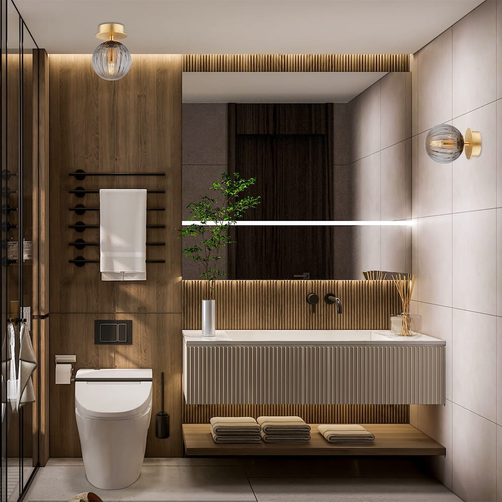 Kinkiet Paloma 1xE14 w kolorze mosiądzu z dymnym kloszem, zamontowany na ścianie w nowoczesnej łazience. Oświetlenie znajduje się obok lustra, otoczone drewnianymi elementami wykończenia.