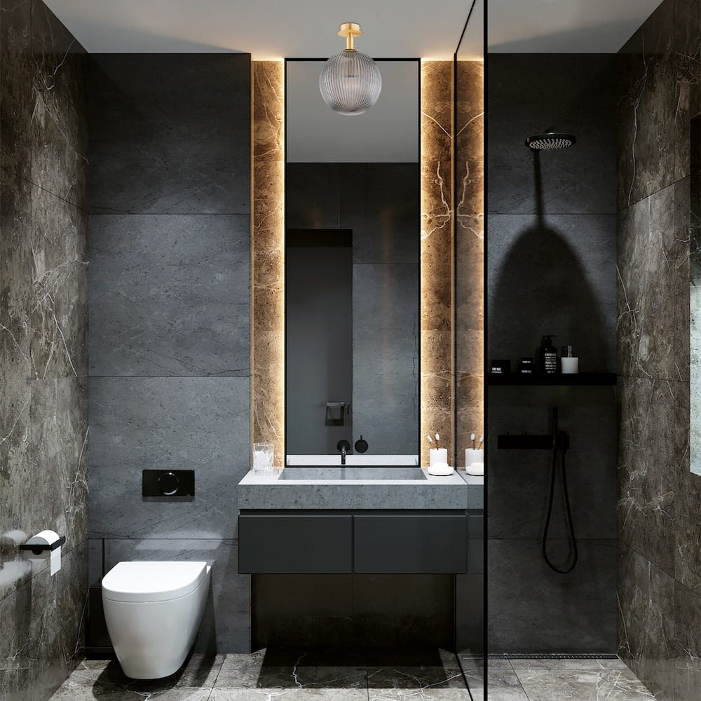 Lampa sufitowa Paloma 1xE27, wykonana z mosiądzu i dymnego szkła, zawieszona w nowoczesnej łazience. Widoczne detale to lekko zaokrąglona, szklana kula oraz metalowe mocowanie w kolorze mosiądzu, oświetlająca lustro i ciemne płytki.