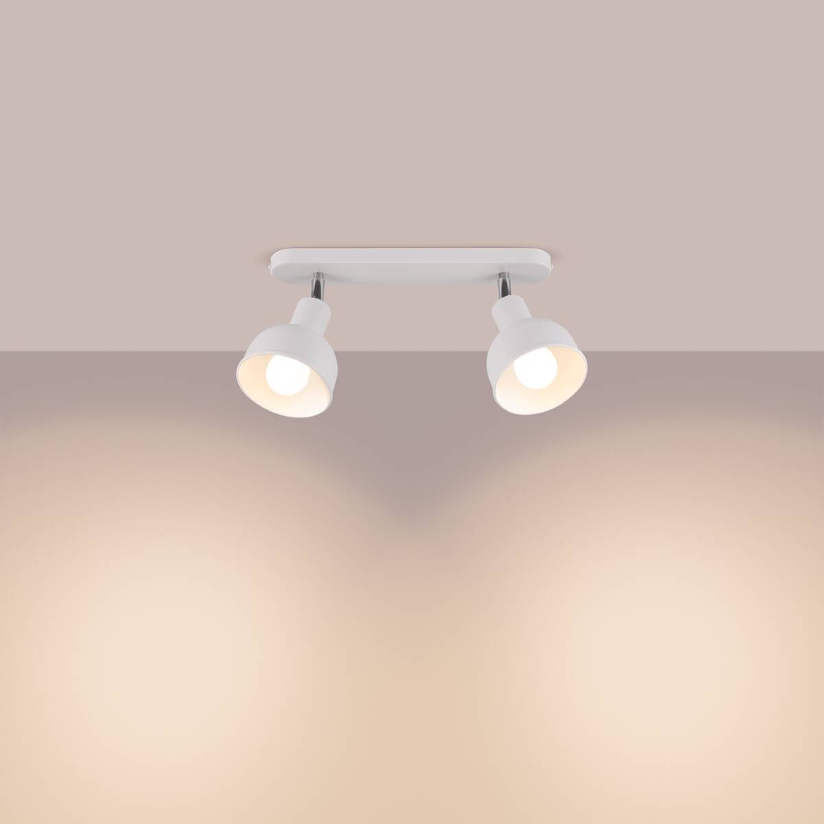 Lampa sufitowa Elba z dwoma reflektorami, biała, z metalowym stelażem. Reflektory skierowane w dół, zamontowane na prostokątnej podstawie. Prosta konstrukcja, idealna do oświetlenia wnętrz. Tło w stonowanym kolorze, podkreślające lampę.