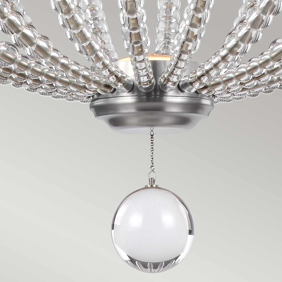 Lampa wisząca Oberlin M w kolorze niklu satynowego z dwiema żarówkami LED 8W. Konstrukcja z błyszczącego metalu z dekoracyjnymi szklanymi elementami, wisząca kula z białego szkła. Produkt zawieszony pod sufitem, z widocznym detalem mocowania.