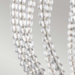 Lampa wisząca Oberlin M z niklu satynowego, z detalami w postaci przezroczystych, szklanych kul o okrągłym kształcie. Kule są ułożone w poziome rzędy, tworząc elegancki design. Na tle gładkiego, szarego tła, lampa prezentuje nowoczesny styl.