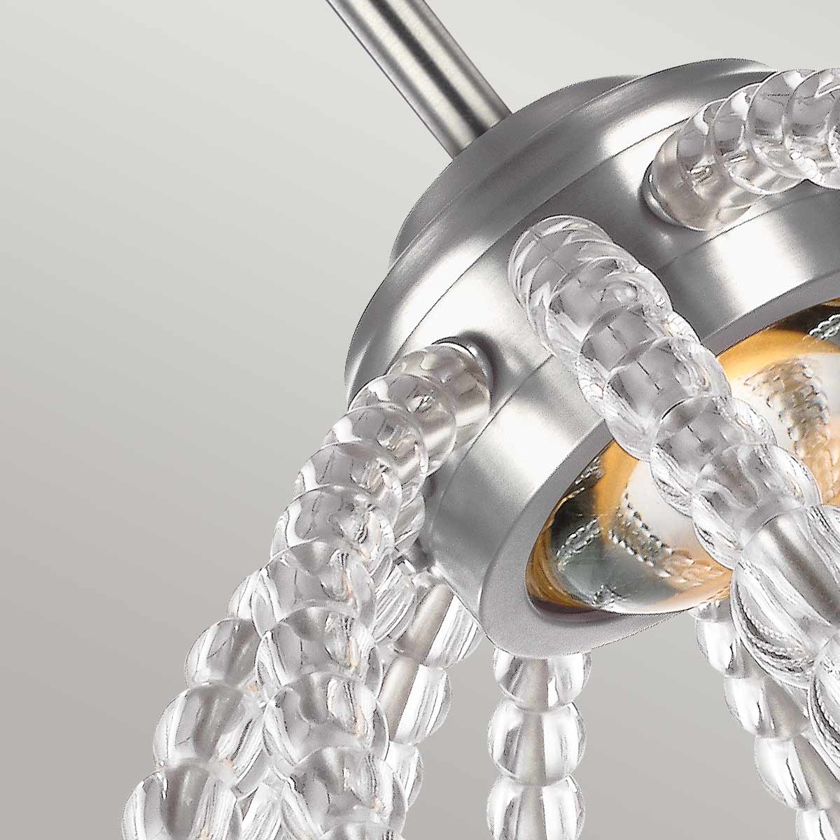 Lampa wisząca Oberlin S z jedną diodą LED 8W, w kolorze nikiel satyna. Wyróżnia się przezroczystymi, szklanymi elementami w kształcie koralików oraz metalowym uchwytem. Zamontowany jest w pozycji wiszącej, zbliżenie na detal mocowania i źródła światła.