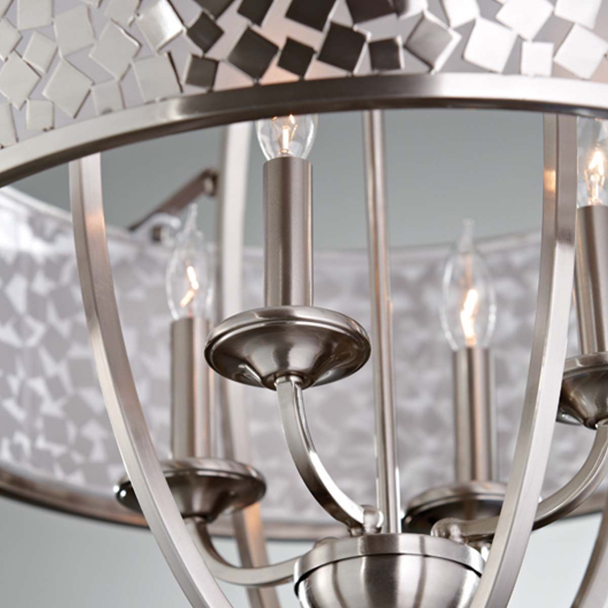 Lampa wisząca Zara 4xE14 w kolorze satynowego niklu. Okrągła, metalowa konstrukcja z czterema miejscami na żarówki, ozdobiona mozaikowym kloszem. Ujęcie z bliska, pokazujące detale mocowań i żarówek. Tło w neutralnym odcieniu.