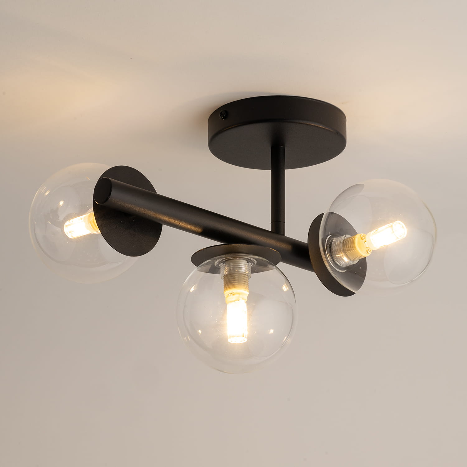 Lampa sufitowa Avola 3xG9 w kolorze czarnym z transparentnymi kloszami. Ułożona w sufit, z trzema okrągłymi kloszami, każdy z widoczną żarówką. Metalowa konstrukcja z matowym wykończeniem, elegancka i nowoczesna.