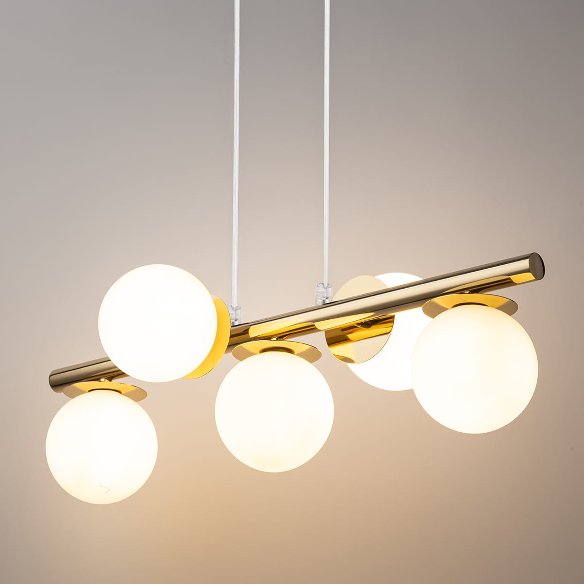 Lampa wisząca Avola 5xG9 w kolorze złotym i białym. Składa się z pięciu okrągłych kloszy z mlecznego szkła zawieszonych na metalowej rurze, z prostymi białymi przewodami. Produkt ma nowoczesny design, idealny do aranżacji wnętrz.