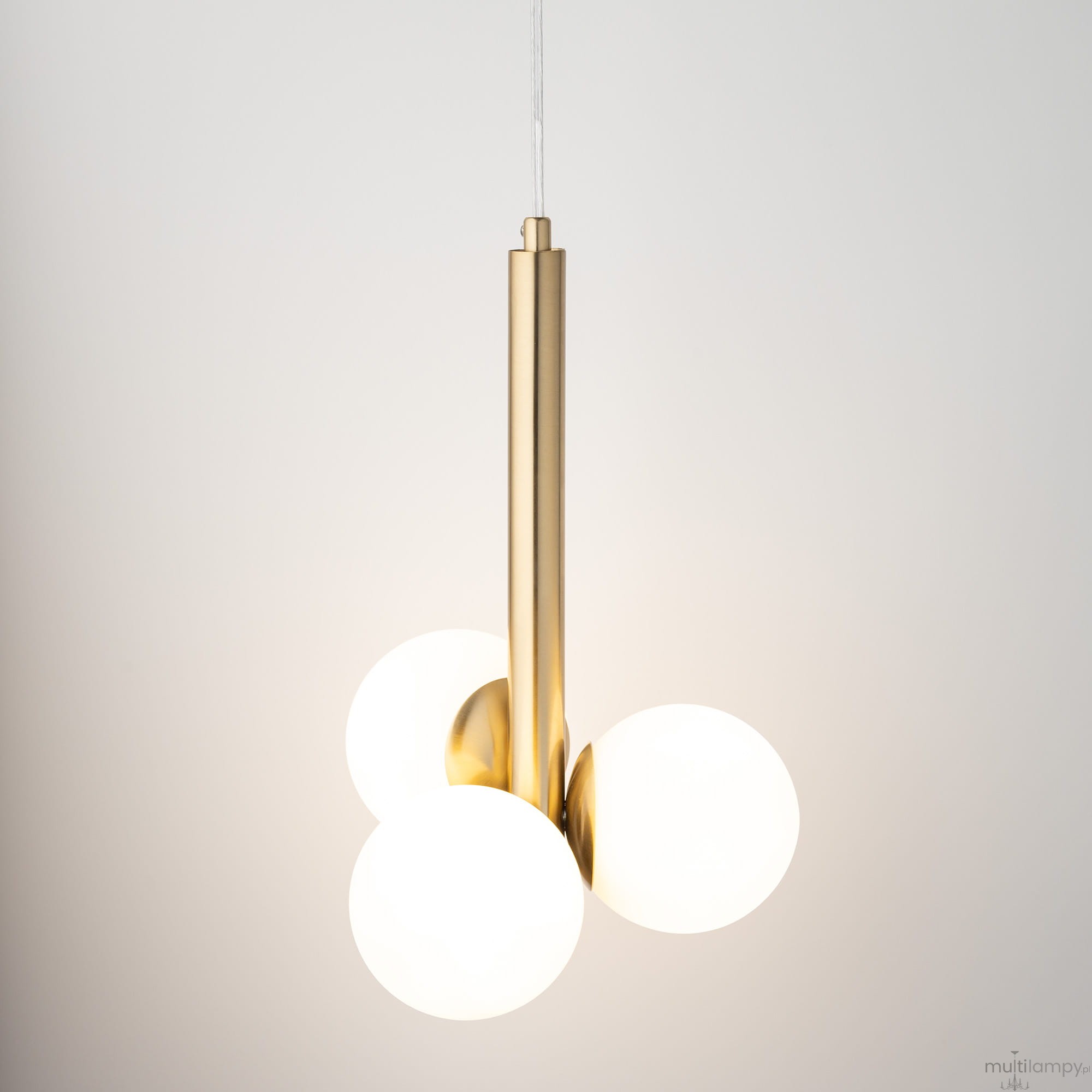 Lampa wisząca Perla Lux 3xG9 w kolorze złotym z białymi kloszami. Trzy okrągłe klosze umieszczone na metalowym, złotym ramieniu. Produkt zawieszony na przezroczystym przewodzie, z minimalistycznym, nowoczesnym designem.