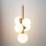 Lampa wisząca Perla Lux z pięcioma kloszami w kształcie białych kul, zawieszona na złotej konstrukcji. Klosze umieszczone blisko siebie, tworzą efektowną kompozycję. Produkt zawieszony na cienkim przewodzie w minimalistycznym, jasnym tle.