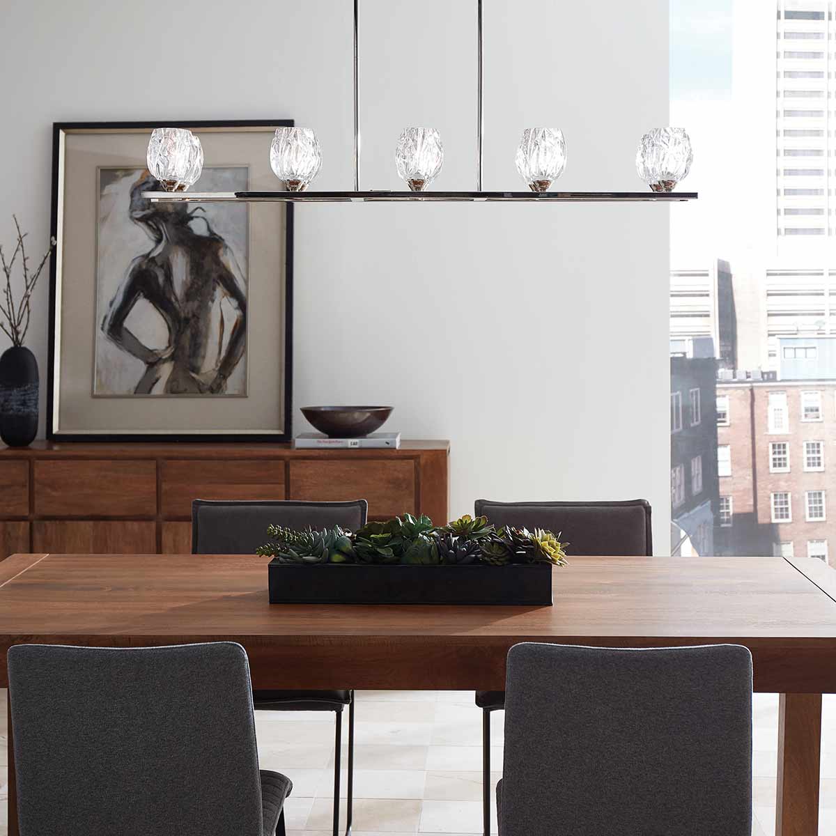 Lampa wisząca Rubin w satynie niklowej z 10 źródłami światła G9, zamontowana nad drewnianym stołem. Szklane klosze o geometrycznym kształcie, w otoczeniu minimalistycznych mebli i dekoracji, tworzą nowoczesne wnętrze.