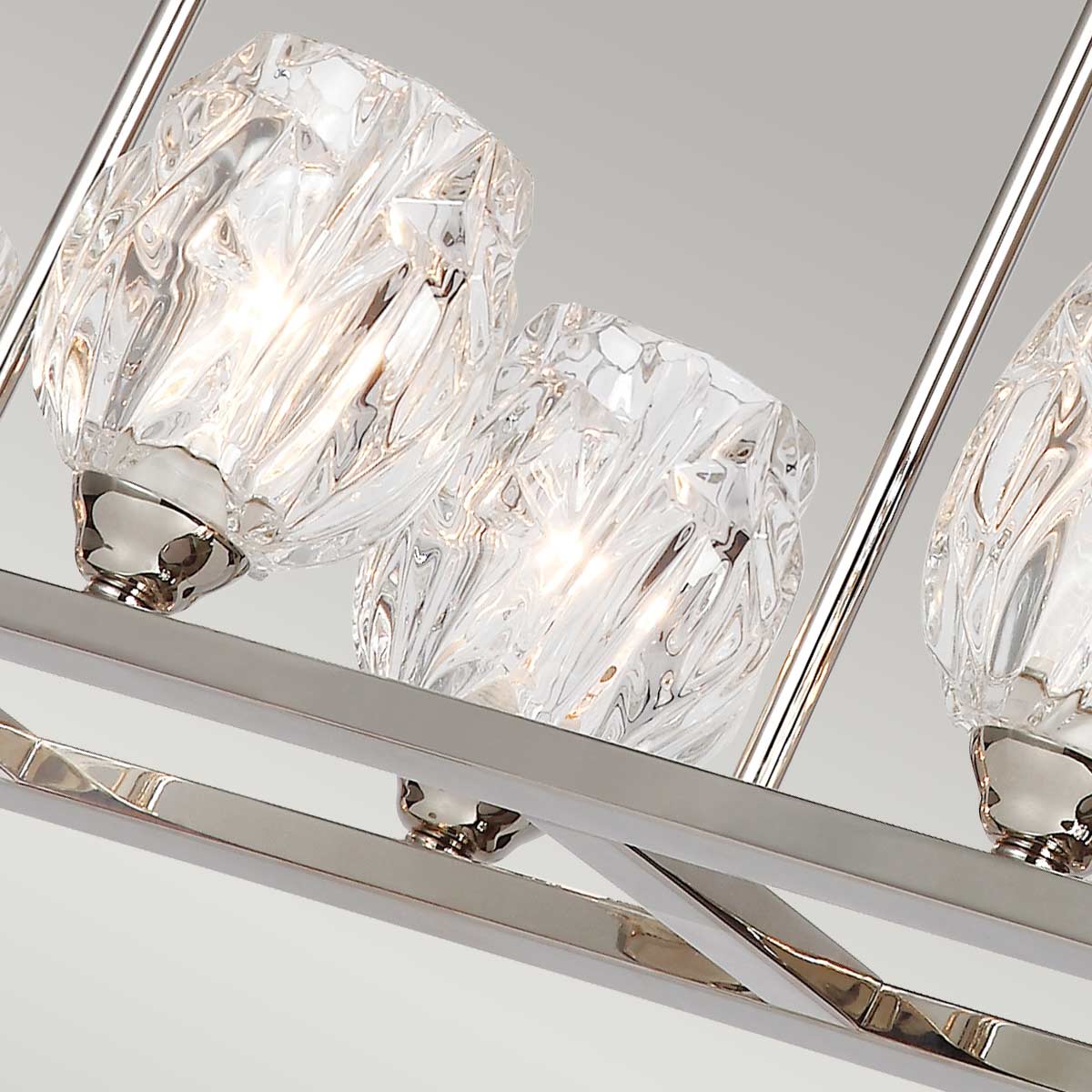 Lampa wisząca Rubin w satynie niklowej z 10 kloszami G9. Klosze mają szklane, przezroczyste, fakturowane wykończenie, które odbija światło. Lampa zawieszona na prostokątnej, metalowej konstrukcji. Ujęcie z góry, ukazujące detale kloszy.