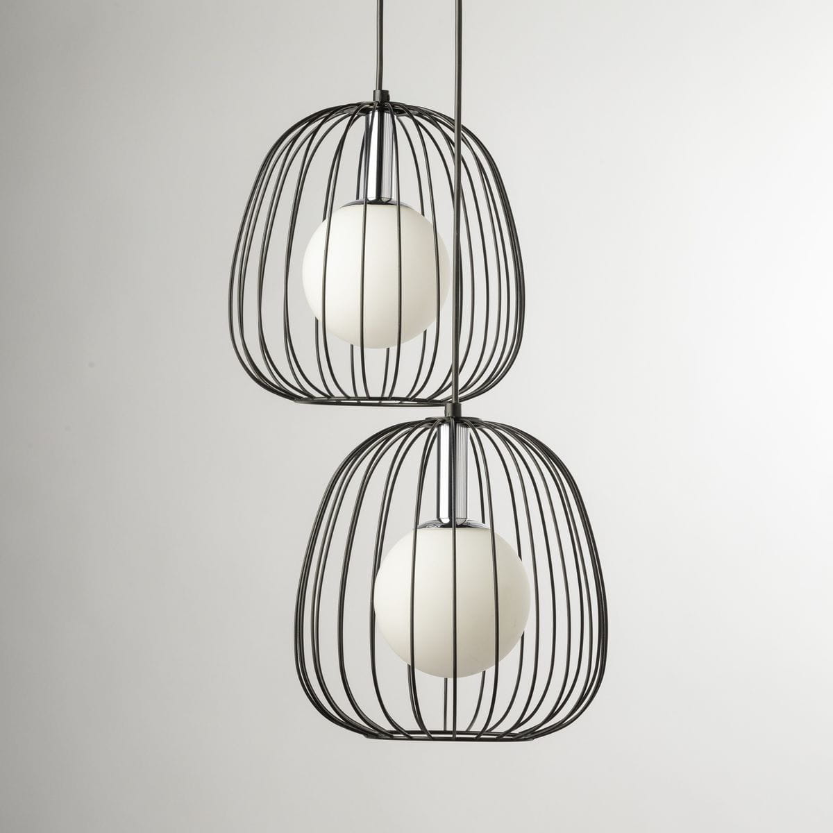 Lampa wisząca Bell z dwiema oprawami G9, w czarnej metalowej klatce z okrągłymi białymi kloszami. Ujęcie z przodu, dwa klosze umieszczone jeden pod drugim, na jasnym tle. Elementy dekoracyjne w minimalistycznym stylu.