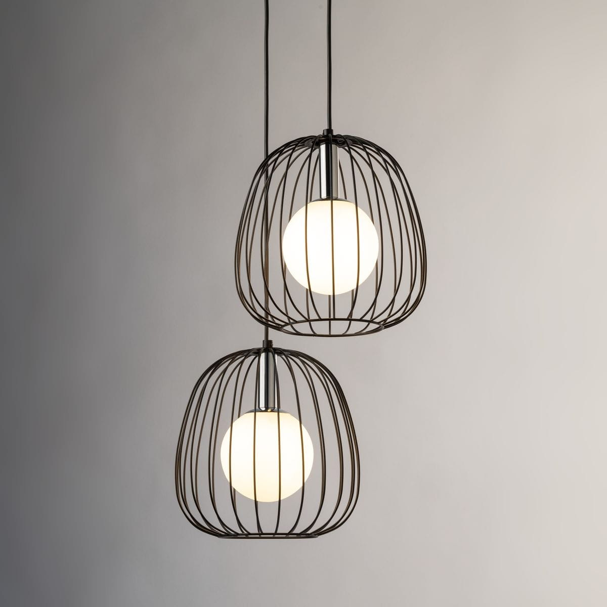 Lampa wisząca Bell w kolorze czarnym i srebrnym, z dwoma okrągłymi kloszami w metalowej siatce. Klosze zawierają białe żarówki G9, wiszące na cienkich linkach. Ujęcie frontalne, na jasnym tle, ukazujące nowoczesny design.