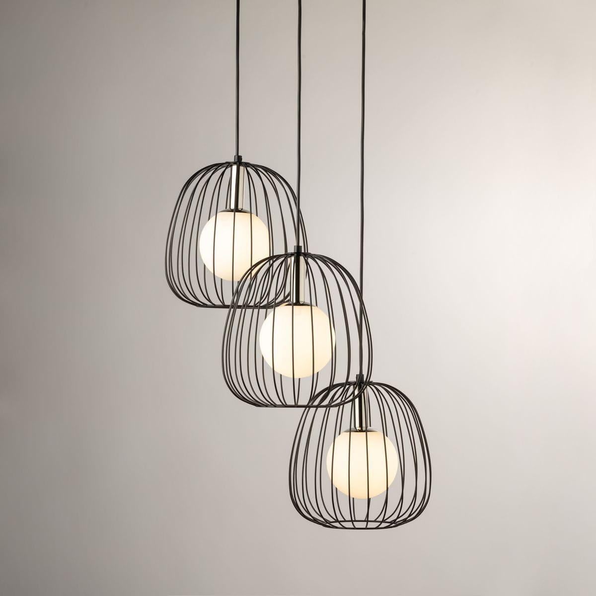 Lampa wisząca Bell z trzema kloszami w formie metalowych siatek w kolorze czarnym, z białymi okrągłymi żarówkami. Produkt zawieszony na cienkich linkach, w minimalistycznym stylu, na jasnym tle.