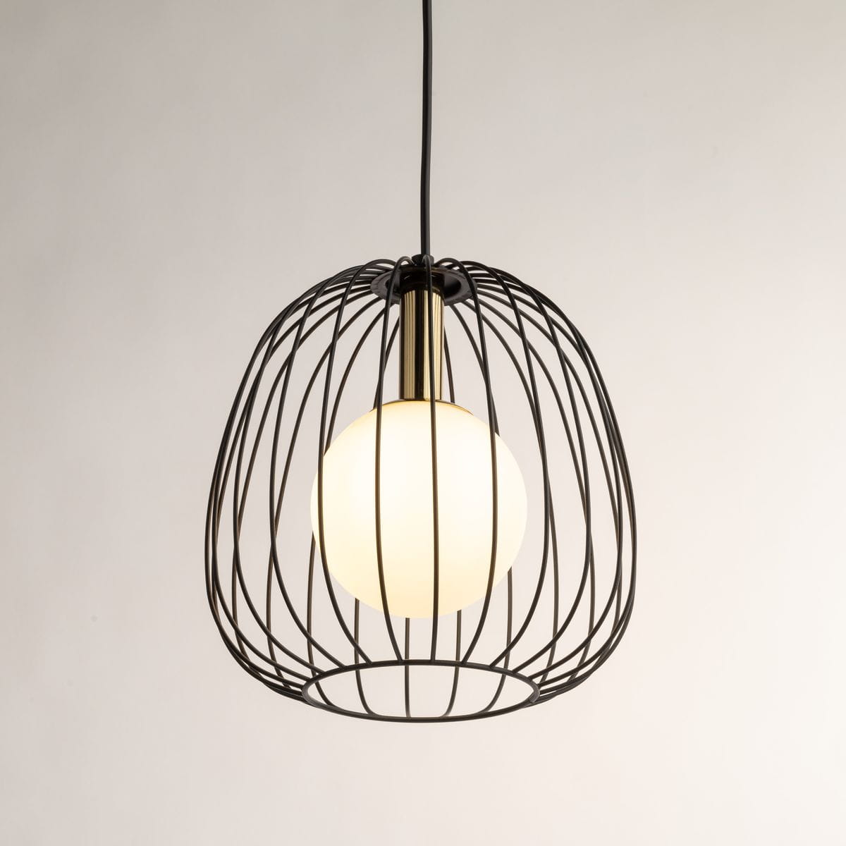 Lampa wisząca Bell D24 z metalowym, czarnym kloszem w formie siatki i złotym uchwytem. Wewnątrz znajduje się okrągła, biała żarówka G9. Ujęcie z góry, lampa zwisa z sufitu na cienkim przewodzie. Tło neutralne, jasne.