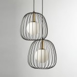 Lampa wisząca Bell z dwoma oprawami G9, w kolorze czarnym i złotym. Posiada metalową klatkę w kształcie owalnym, w której znajdują się białe, okrągłe klosze. Zawieszona na cienkich linkach, prezentuje nowoczesny design. Tło neutralne, jasne.