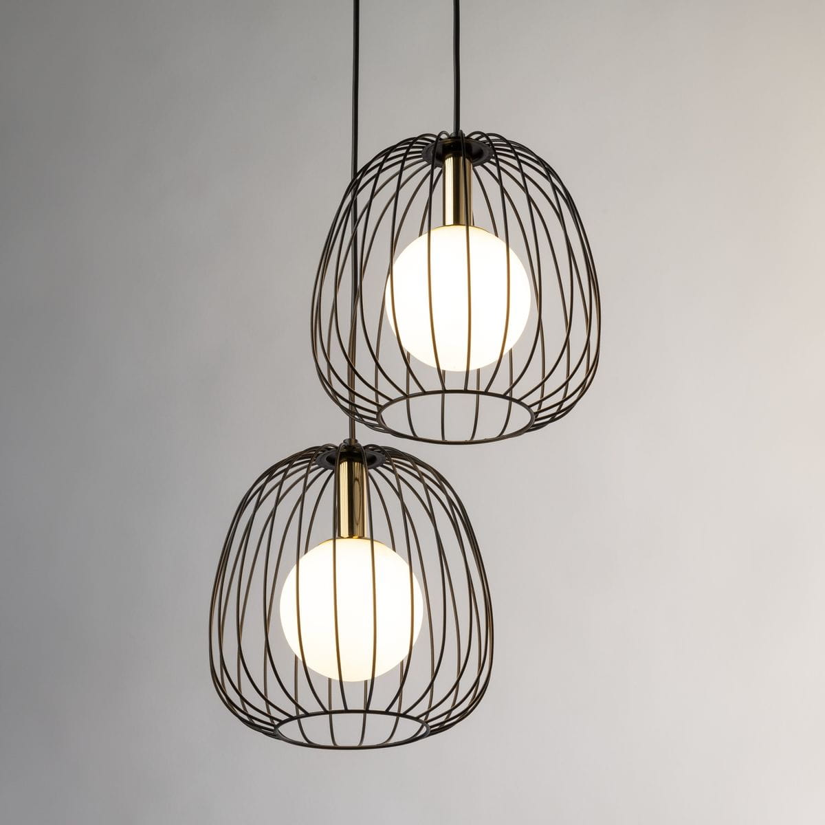 Lampa wisząca Bell z podwójnym kloszem w kolorze czarnym i złotym, z okrągłymi, białymi żarówkami w metalowej siatce. Ujęcie frontalne, zawieszona na dwóch cienkich linkach, na jasnym tle.