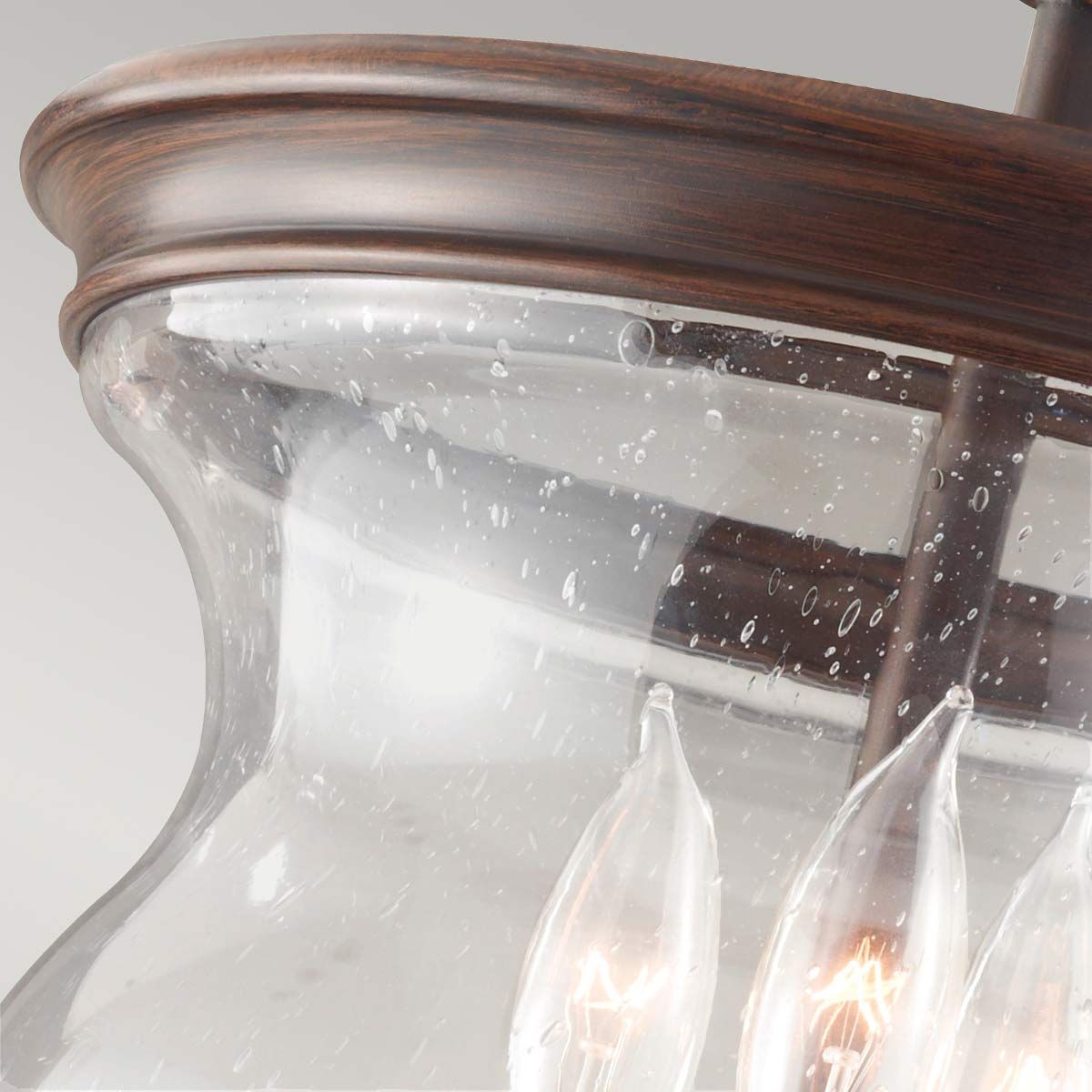 Lampa sufitowa Pickering w kolorze starym brązie, z przezroczystym kloszem o falistym kształcie, widoczne trzy żarówki E14. Klosz z drobnymi bąbelkami, montowany na metalowej konstrukcji. Ujęcie z góry, na jednolitym tle.