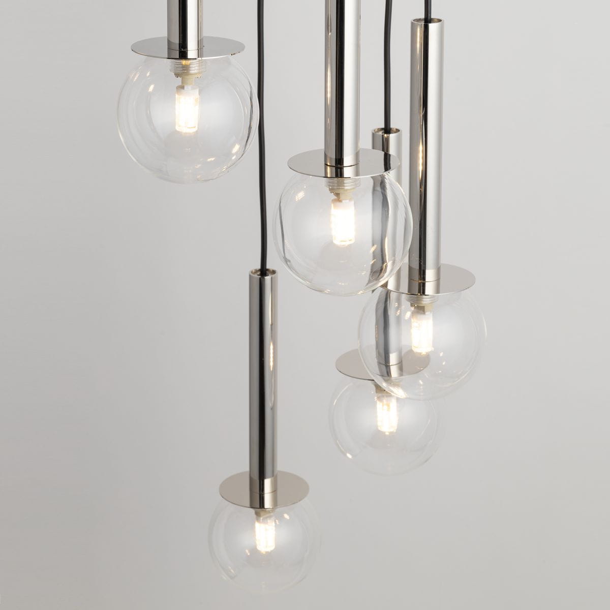 Lampa wisząca Daisy z 7 kulami G9 w kolorze srebrnym i transparentnym. Wysokie, cylindryczne elementy metalowe z połyskiem, podtrzymujące szklane klosze. Zbliżenie na detale, z widocznymi źródłami światła w każdej kuli. Tło jednolite.
