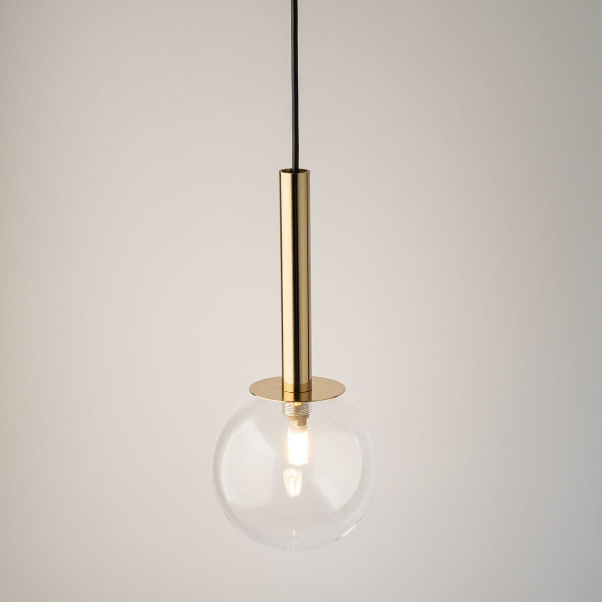 Lampa wisząca Daisy z przezroczystym kloszem w kształcie kuli i złotym metalowym uchwytem. Zawieszona na czarnym przewodzie, prezentuje minimalistyczny design, idealna do nowoczesnych wnętrz.