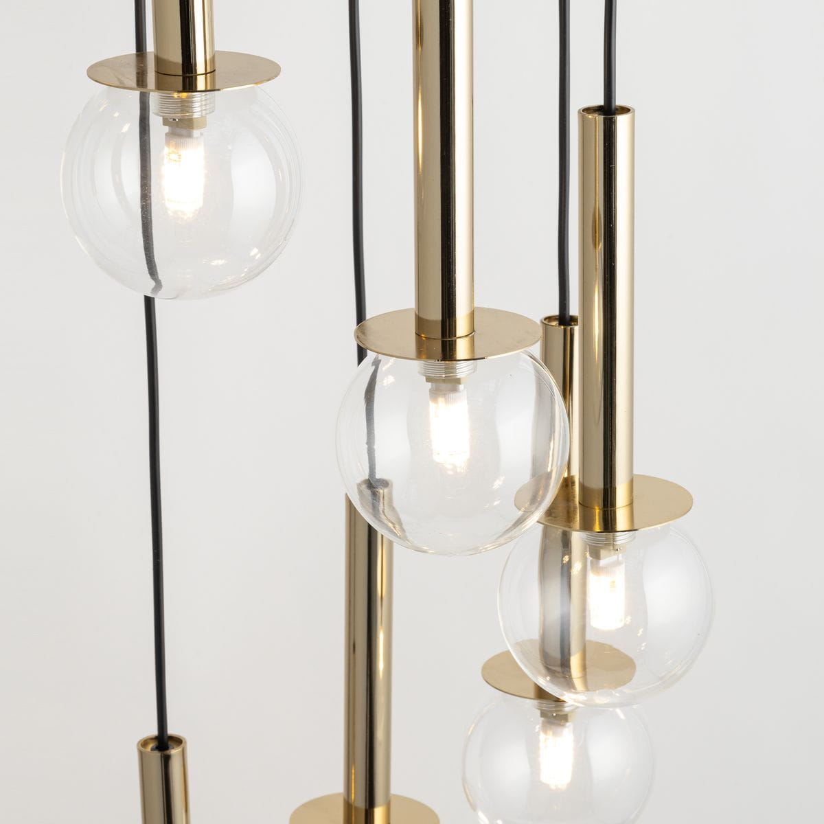 Lampa wisząca Daisy z pięcioma kloszami G9, w kolorze złotym i transparentnym. Klosze w formie kul z przezroczystego szkła zawieszone na złotych rurkach. Ujęcie z góry, pokazujące szczegóły konstrukcji i źródła światła.