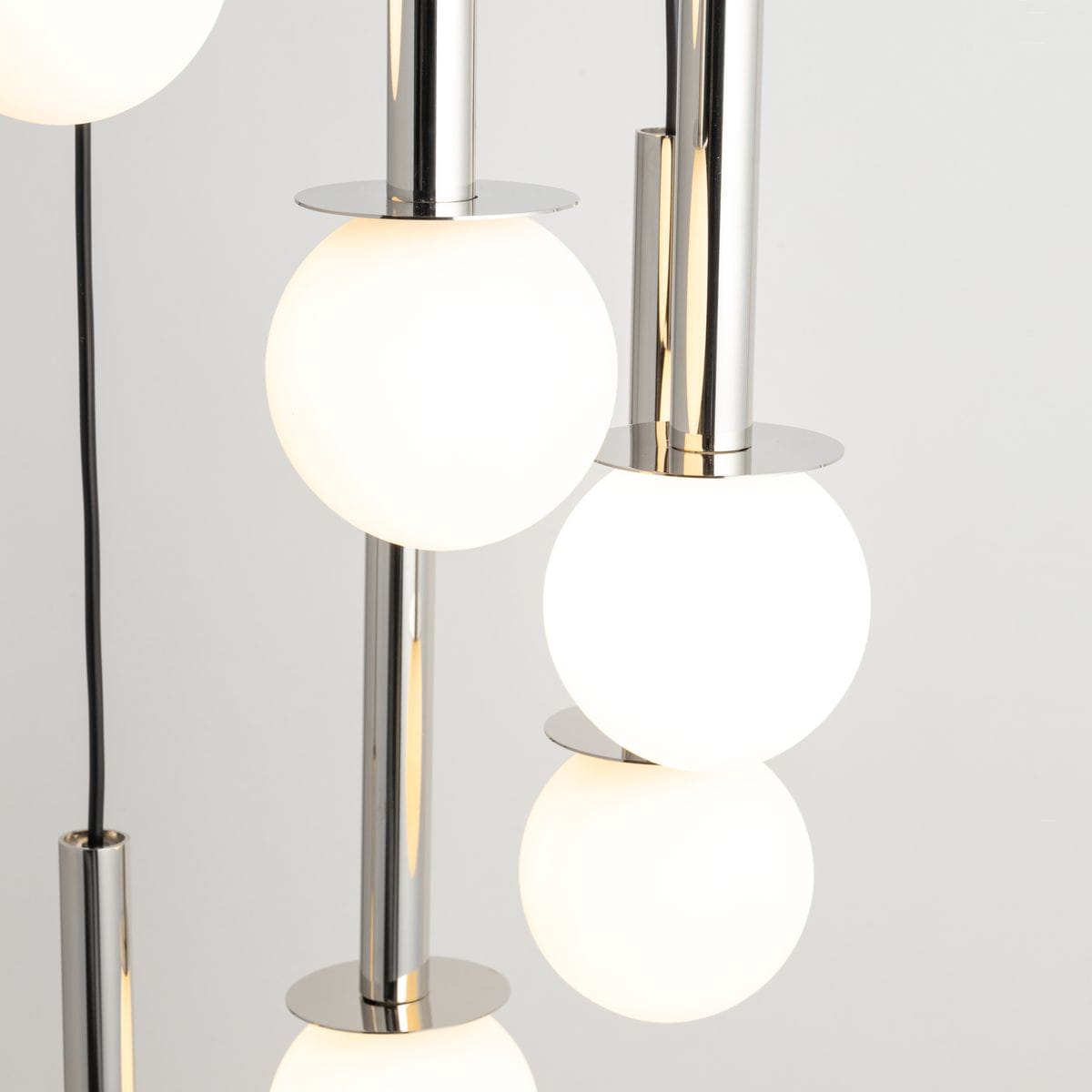 Lampa wisząca Daisy z 7 kulami G9. Srebrne metalowe elementy i białe, matowe klosze w kształcie kul. Ujęcie zbliżeniowe, ukazujące detale konstrukcji i połączenia między elementami. Tło w jasnym odcieniu.