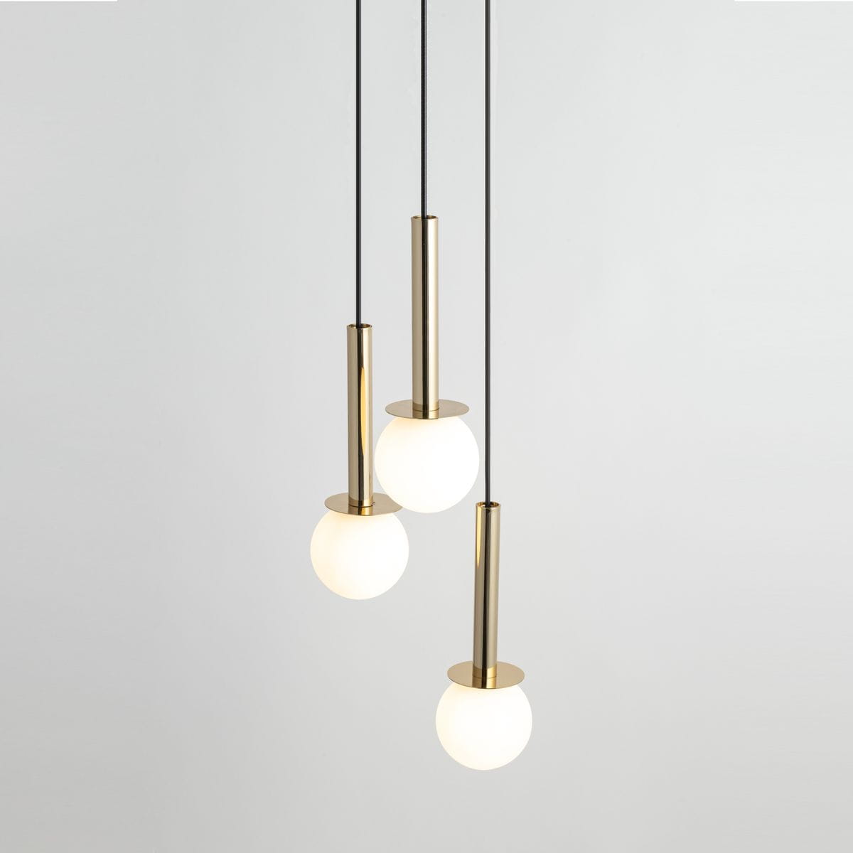 Lampa wisząca Daisy 3xG9 w złotym i białym kolorze, składająca się z trzech okrągłych kloszy z mlecznego szkła zawieszonych na cienkich czarnych linkach. Klosze umieszczone na cylindrycznych podstawach z połyskującego metalu.
